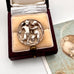 Antique silver button with relief sculpture in a wooden box on a white surface.