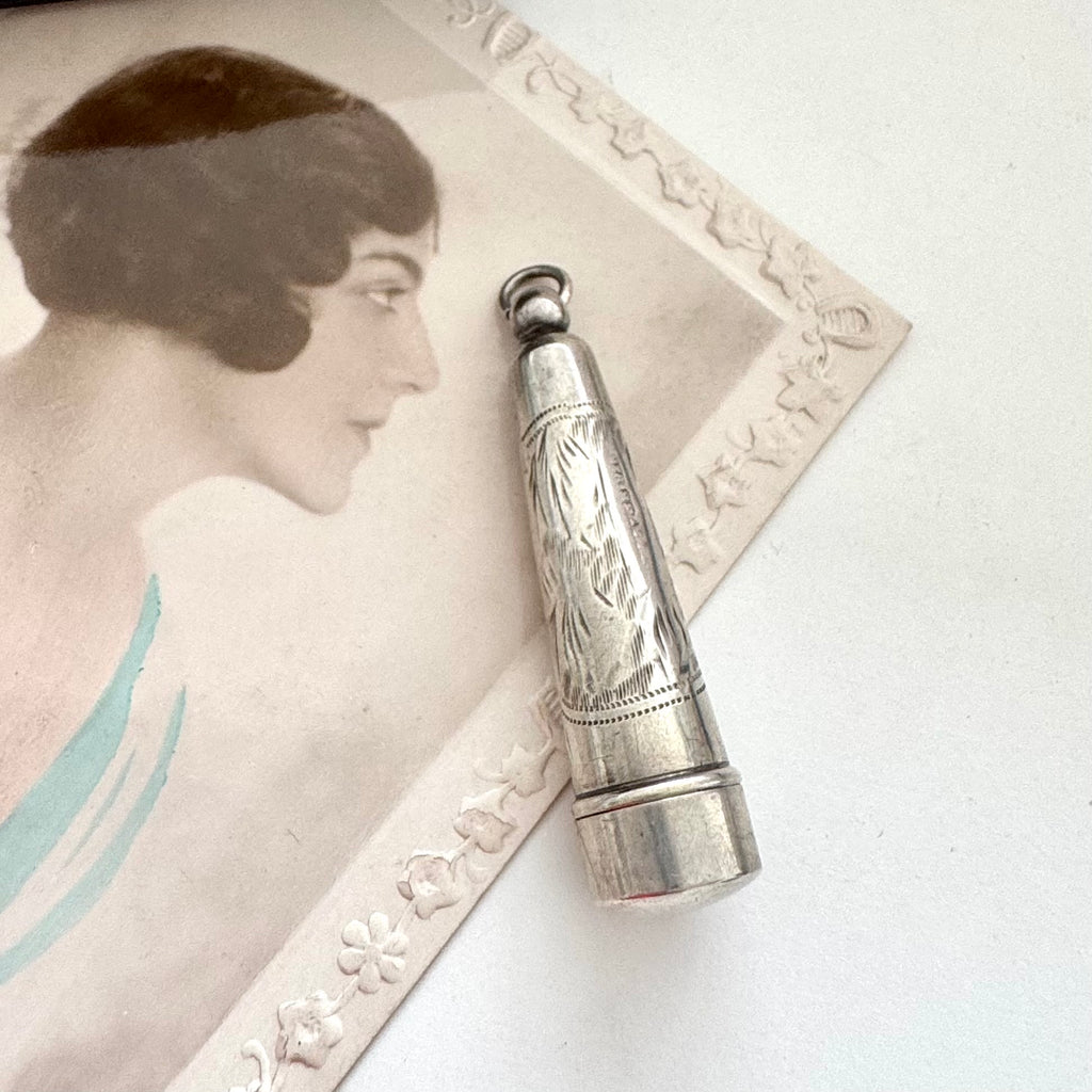 Antique silver cheroot holder case on an old postcard of a woman.