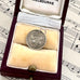 Silver antique threepence coin charm with a purple gemstone in an open jewelry box on sheet music.