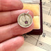 Silver coin pendant with a purple gemstone held between fingers on sheet music.