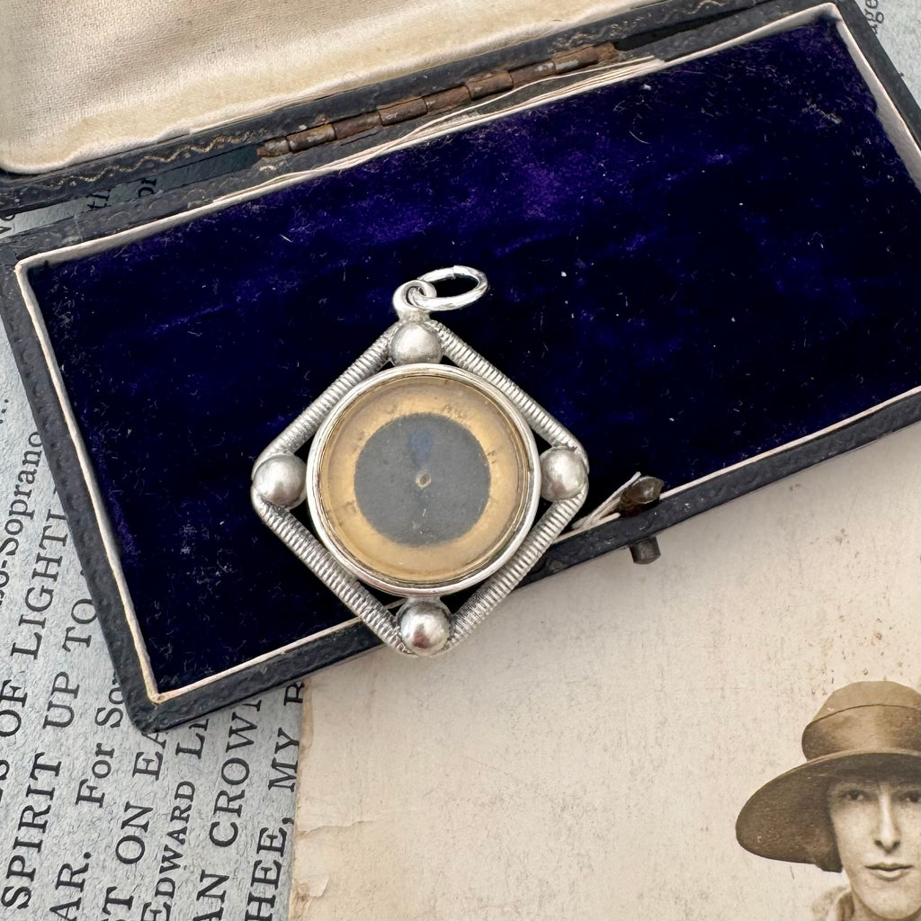 Antique silver compass watch fob with a displayed on an old photograph and text.