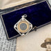 Antique silver compass watch fob with a displayed on an old photograph and text.