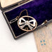 Antique silver bow brooch in an open jewelry box with a purple interior.
