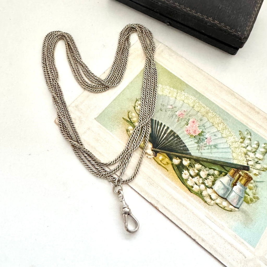 Antique silver guard chain necklace on a decorative card with a fan and bottle illustration