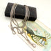 Antique silver guard chain necklace on an old jewellery box and decorative card with a fan and bottle illustration