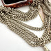 A close-up of a silver plated guard chain necklace draped across a white surface, with part of a brown marbled object visible in the upper left corner.