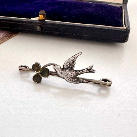 Antique silver brooch with bird and clover design on a white surface