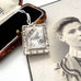 An antique aesthetic era rectangular silver locket with an engraved bird and reeds design, displayed next to its vintage presentation box on top of an antique black-and-white portrait photograph.