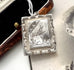 An antique Victorian rectangular silver pendant necklace featuring an engraved bird and reeds, resting on a light surface next to an open vintage wooden box.