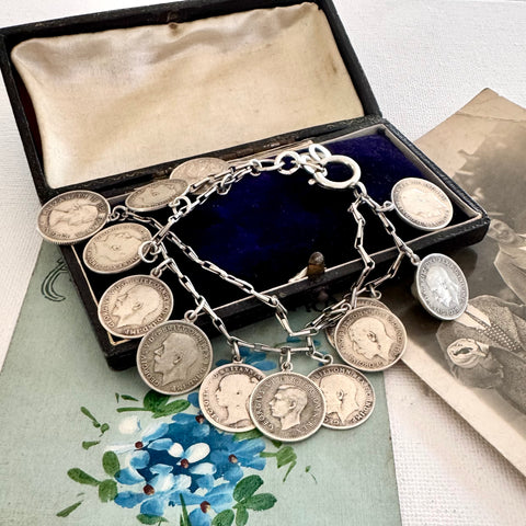Silver coin bracelet with antique British threepence coins in an open jewelry box on a floral surface.