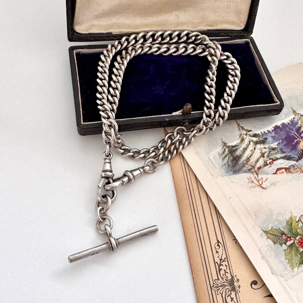 Antique silver watch chain necklace with a clasp on an open jewelry box with vintage cards underneath.