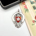 Antique silver and red enamel watch fob on a white background and with a vintage postcard