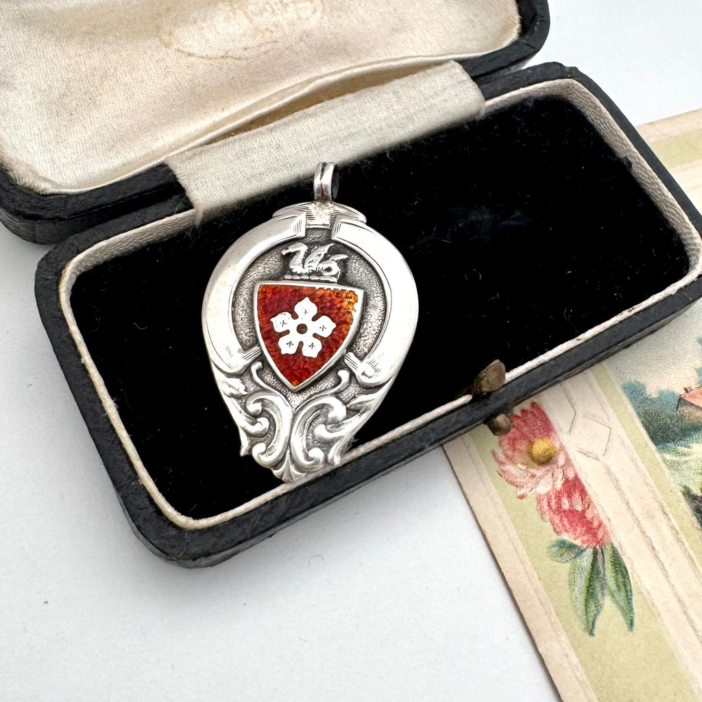 Antique silver and red enamel watch fob on an open jewellery box.