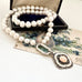 Pearl and antique 1928 watch fob necklace with a silver clasp on an open jewelry box with floral card in the background