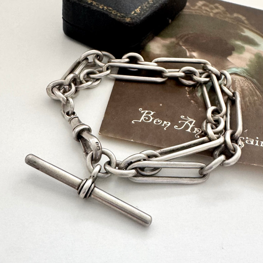 Antique silver trombone chain bracelet on a white surface with a vintage-style card in the background.