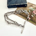Antique sterling silver trombone chain link bracelet with clasp on a white surface with an old book and floral illustration in the background.