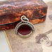 Antique victorian albo silver carnelian and bloodstone spinning fob displayed on top of a vintage sepia-toned photograph and a vintage jewellery box.