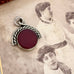 A Victorian albo silver spinning fob with a round deep red center, placed on top of an old sepia-toned photograph of two women.