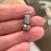 A small antique wax seal fob pendant or charm with engraved vertical leaf-like patterns and a loop at the top, shown resting on a person's fingers against a blurred background.