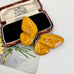 An amber-yellow  Art Deco era butterfly-shaped brooch with green and orange speckles and a black thorax, displayed on top of an open vintage presentation box with a floral card underneath.