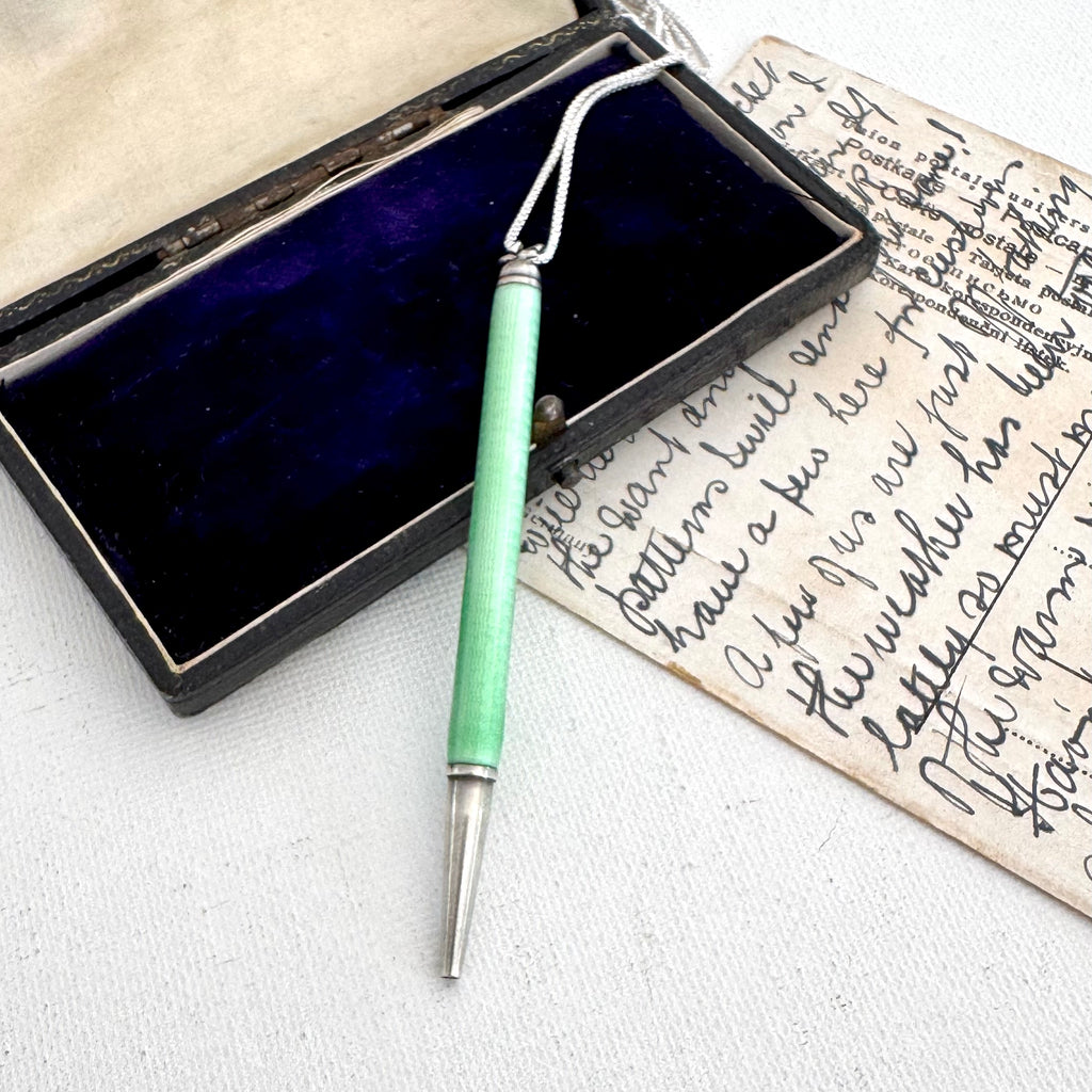 Art Deco silver and guilloche enamel propelling pencil resting inside an open dark velvet box next to an old handwritten letter on aged paper.