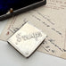 Silver stamp holder with 'STAMPS' engraved on it, placed on an old letter.