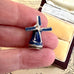 Small windmill-shaped pendant held between fingers with a vintage box in the background