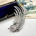 Decorative silver bird brooch with intricate design on a white surface with floral background