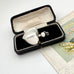 Silver heart-shaped perfume bottle pendant in an open black jewelry box on a white surface.