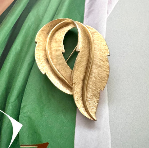 Crown Trifari Gold leaf-shaped brooch on a green and white fabric background