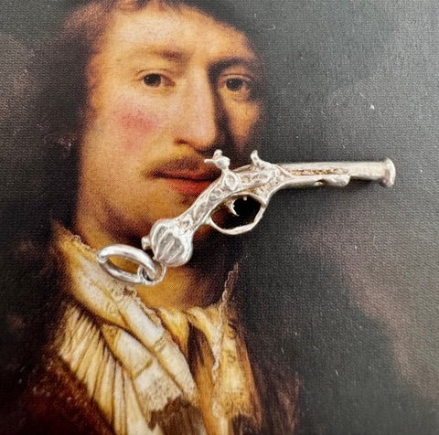 Vonk Jewellery silver flintlock pistol charm on a picture of an old master painting of a man.