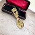 Decorative gold over silver Sami spoon with intricate designs in a black case on a paper with music notes on it.