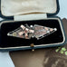 Victorian 1900 antique sterling silver and rose gold sweetheart brooch with the words 'BEST WISHES' in raised lettering, styled on a vintage jewellery box