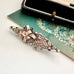 Victorian 1900 antique sterling silver and rose gold sweetheart brooch with the words 'BEST WISHES' in raised lettering, styled on a floral green card next to a vintage black case.