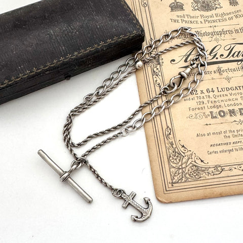 Antique silver albertina chain necklace with an anchor pendant on a vintage box and antique advertising material. 