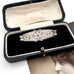 Victorian silver floral sweetheart brooch displayed inside an open black velvet jewelry box with a cream lining, with a vintage portrait card partially visible underneath.
