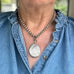 Person wearing a Victorian silver necklace with a pendant, visible under a blue denim shirt.
