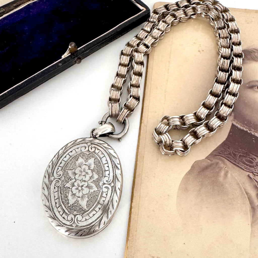Victorian silver belcher chain with a decorative locket on a white surface next to an old photograph.
