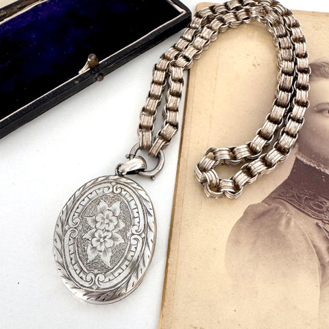 Victorian silver belcher chain with a decorative locket on a white surface next to an old photograph.