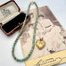 A vintage turquoise and gold heart pendant necklace is displayed on top of an antique sepia-toned portrait photograph and an open vintage jewelry box.