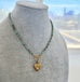 A beaded necklace with turquoise and brown beads, gold-toned metal links, and a vintage Carl Art gold heart-shaped pendant, displayed on a gray fabric jewelry bust.
