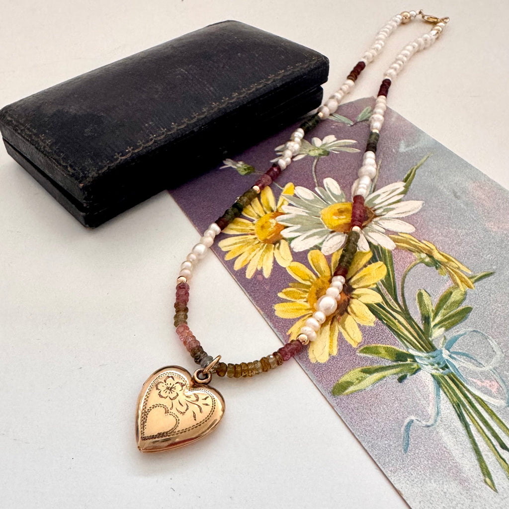 Vintage rolled gold Varga heart locket and tourmaline and pearls necklace on a vintage postcard and with an old jewellery box