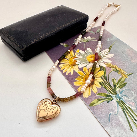 Vintage rolled gold Varga heart locket and tourmaline and pearls necklace on a vintage postcard and with an old jewellery box