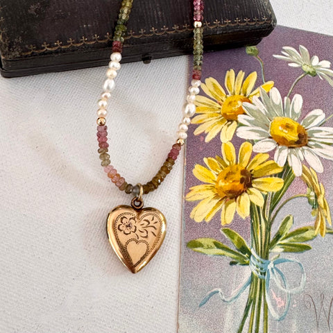 Necklace with a vintage Vargas heart locket on a surface with flowers and a book in the background