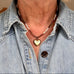 Person wearing a denim shirt with a necklace featuring a heart-shaped pendant.
