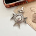 An antique sterling silver star-shaped watch fob with a circular center medallion engraved with 'SCHOOL OF ARMS' displayed on a vintage photograph next to an old wooden box.