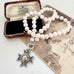 An antique sterling silver star-shaped watch fob with a circular center medallion engraved with 'SCHOOL OF ARMS' on a pearl necklace and displayed on a vintage photograph next to an old wooden box.