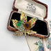 A vintage European hand wired gold-toned brooch shaped like a lotus flower with green, amber, and multicolor rhinestone accents, displayed inside an open wooden jewelry box with cream lining.