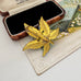 Back of vintage European floral brooch displayed next to an open vintage wooden jewelry box on a beige textured paper surface.