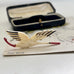A vintage 1930's flying stork brooch or pin with cream-colored body and wings, black feather accents, and a red beak, displayed on a printed card with an open dark case in the background. 